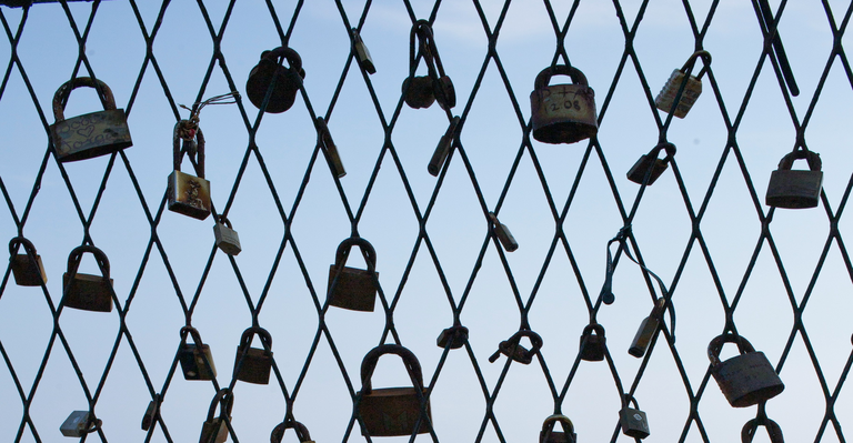 Vorhängeschlösser an einem Gitterzaun vor blauem Himmel als Symbol für Schutz und Sicherheit.