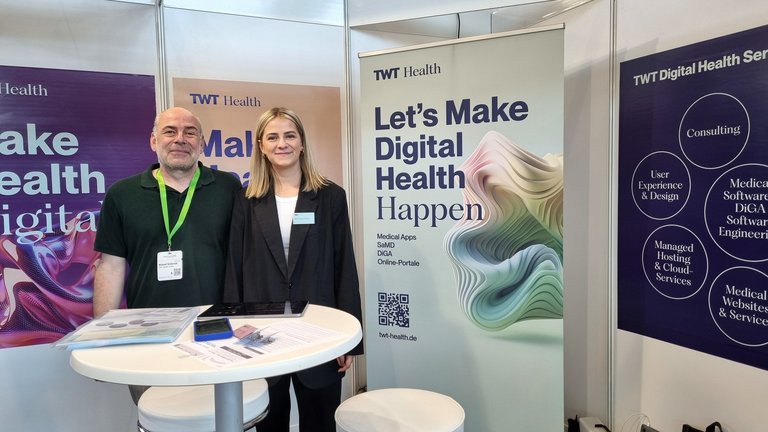 Michael Grüterich und Betty Farrenkothen stehen nebeneinander am Messestand auf der MedtecLIVE in Stuttgart.