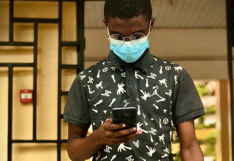Porträt eines Mannes, der eine Gesichtsmaske und eine Brille trägt und dabei auf das Smartphone in seiner Hand schaut.
