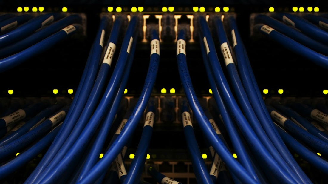 Netzwerk-Server mit blauen Ethernet-Kabeln und leuchtenden Statusanzeigen – Symbol für sicheres Hosting und Dateninfrastruktur im Gesundheitswesen.